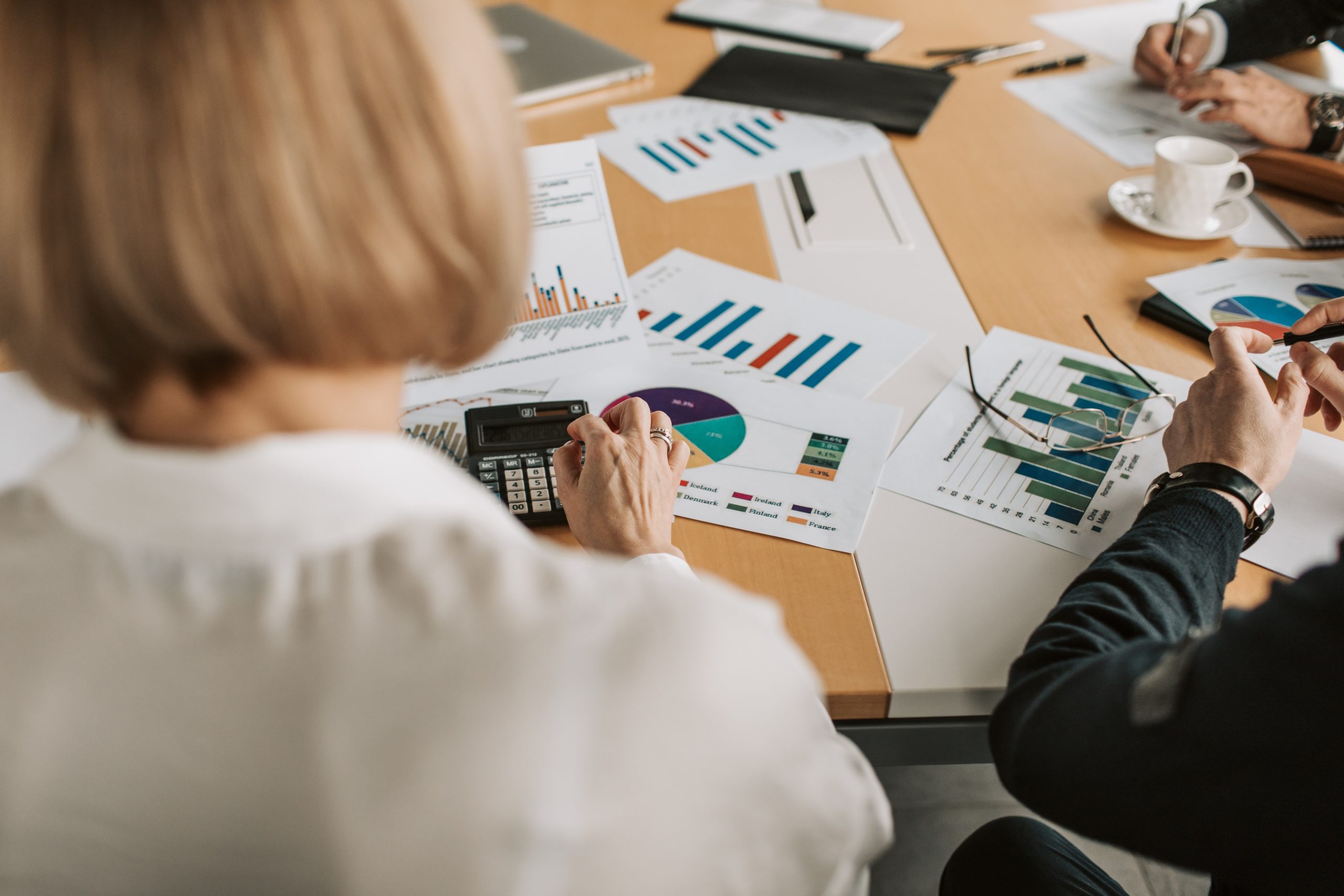 Business Analysis Meeting A blonde woman in a white blouse sits in front of a desk that has important documents scattered across it's surface